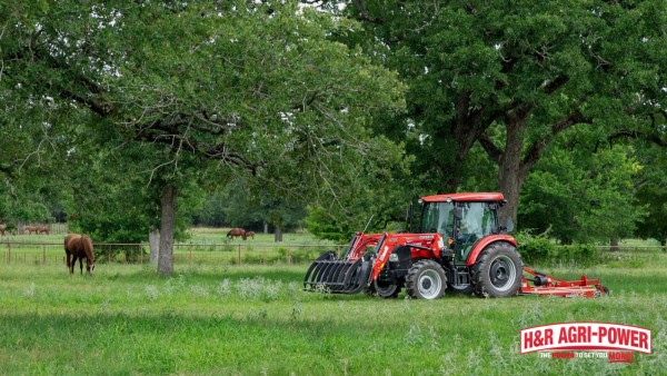 Case IH tractor mowing pasture near livestock with rotary cutter and front grapple attachment
