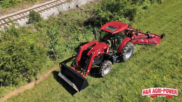 Case IH tractor with rotary cutter mowing along a field edge near railroad tracks