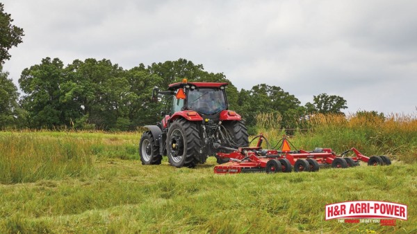 Case IH tractor using rotary cutter to clear tall roadside grass and overgrown vegetation