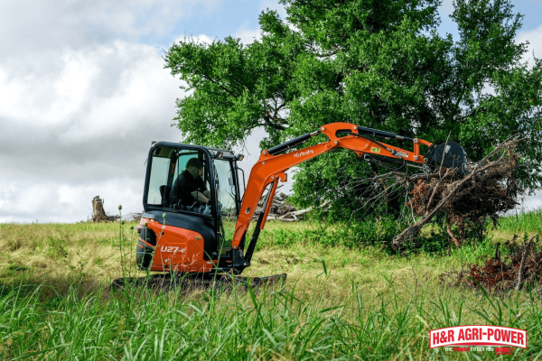 Kubota compact excavator using hydraulic thumb attachment to lift and move brush on a farm