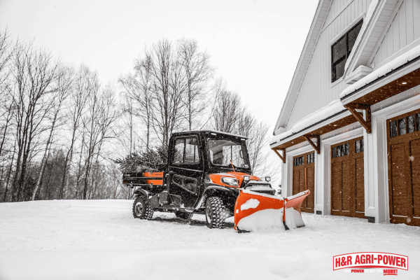 Kubota RTV utility vehicle with snow plow attachment clearing driveway during winter conditions