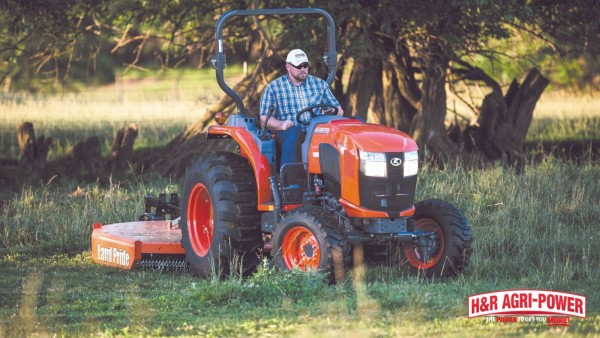 Kubota tractor operating a Land Pride cutter through tall grass near trees