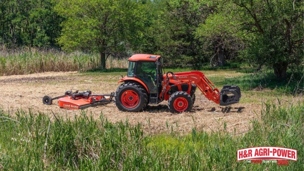 Kubota tractor using a Land Pride rotary cutter to mow rough vegetation near a wooded area