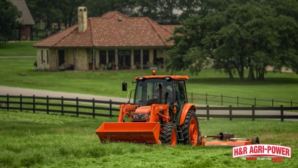 Kubota tractor mowing a rural field near a home and fenced pasture