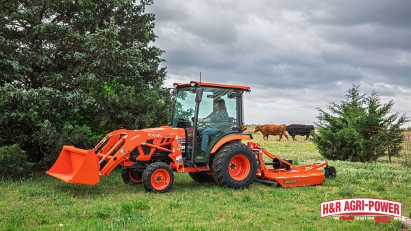 Kubota tractor with rotary cutter mowing pasture grass near livestock and trees