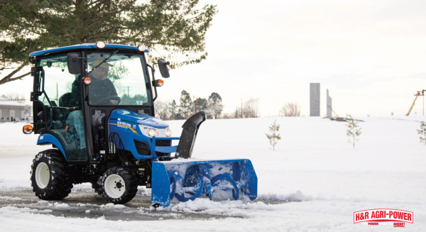 New Holland compact tractor with snow blower attachment clearing driveway on small acreage property