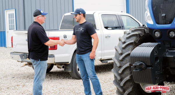New Holland dealer and customer shaking hands beside tractor, reflecting ongoing training and innovation updates