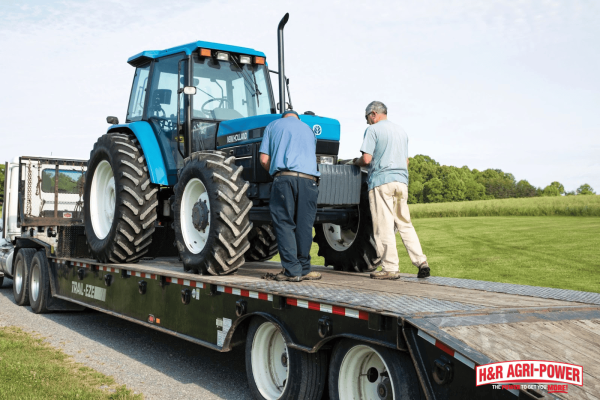Technicians inspecting a New Holland tractor on a trailer, emphasizing the importance of regular service intervals