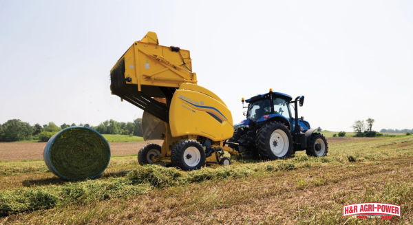 New Holland round baler operating in hay field forming round bale during safe harvesting operation