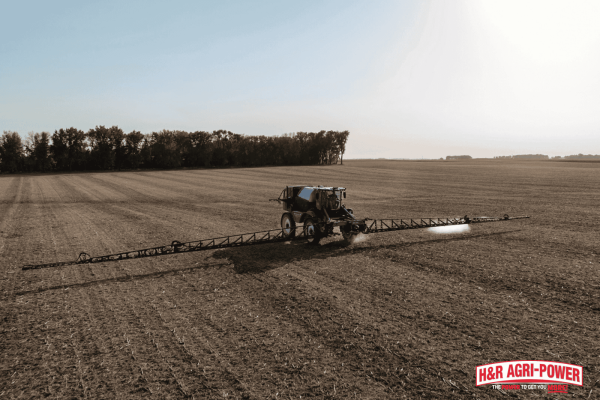 New Holland sprayer operating across a large field, showcasing professional support and equipment solutions from H&R Agri-Power
