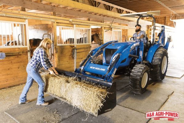 New Holland tractor operating inside a barn while feeding hay, demonstrating cab visibility and control features in confined spaces