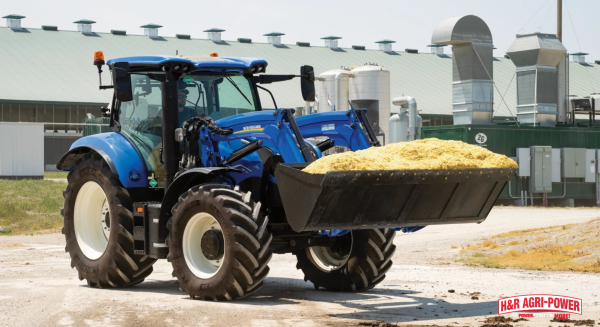 New Holland tractor with front loader carrying silage near farm facility, demonstrating durability and long-term reliability