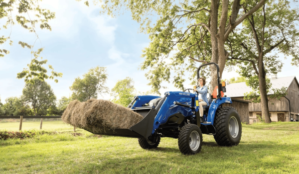 New Holland compact tractor using front loader to move hay demonstrating attachment versatility