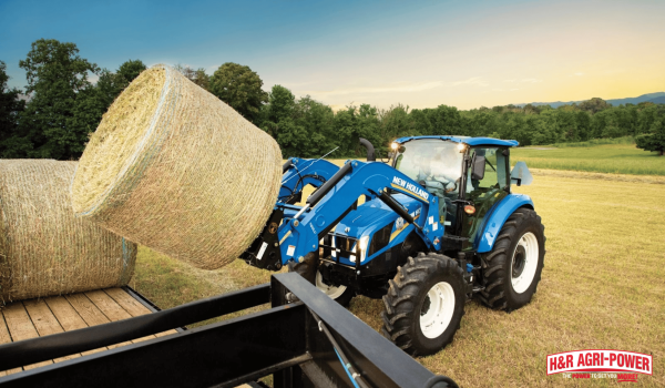 New Holland tractor using front loader to move hay representing regular equipment checks and maintenance