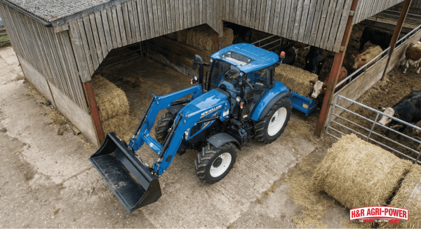 New Holland T5 tractor maneuvering into a livestock shed with a front loader attached.