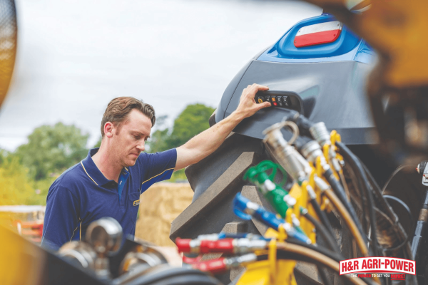 Technician inspecting tractor hydraulic controls and system components, preparing equipment for hydraulic bleeding