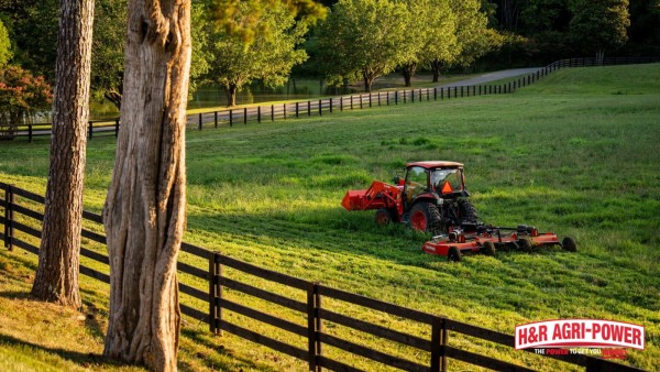 Tractor using a rotary cutter to mow pasture grass near a fence line