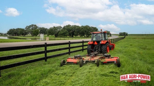 Tractor with rotary cutter mowing grass along a fence line near open pasture