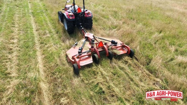 Tractor mowing uneven tall grass with a rotary cutter showing rough cutting performance