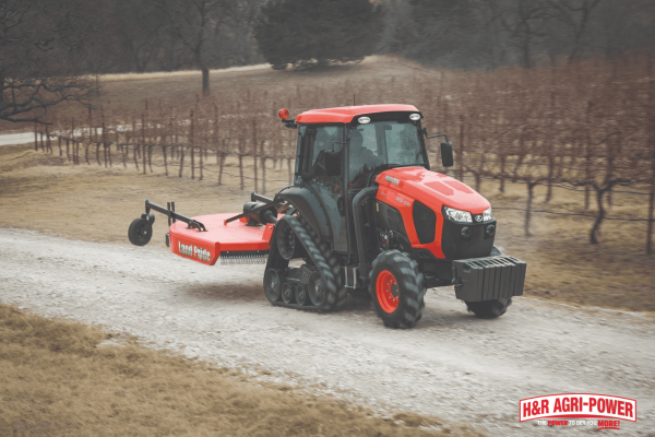 Kubota M5N driver-optional tractor mowing orchard rows, demonstrating autonomous operation for specialty crop growers seeking higher productivity and reduced labor reliance.